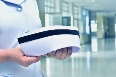 Midsection of female nurse holding headwear in corridor at hospital