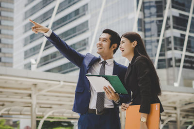 Businessman pointing while standing with businesswoman against building