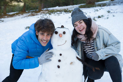 Portrait of young couple with snowman during winter
