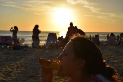 Close-up of young woman eating food at beach during sunset