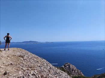 Man standing on rock by sea against blue sky