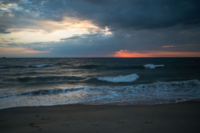 Scenic view of sea and crashing waves against sky during stormy sunrise