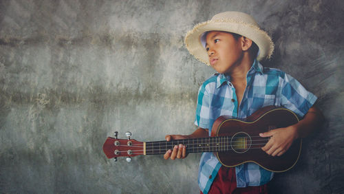 Boy playing guitar against wall