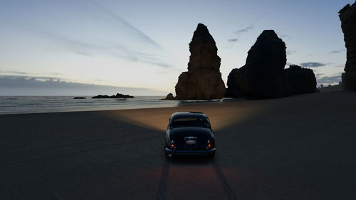 Cars on rocks at beach against sky during sunset