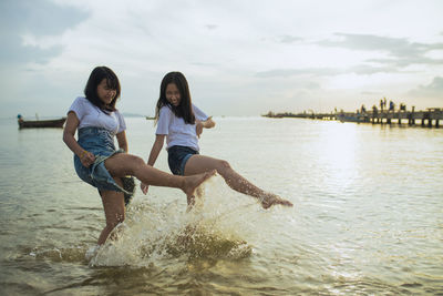 Friends splashing water in sea against sky