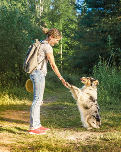 Playful trained mixed breed dog giving paw to happy middle aged woman during walk in park