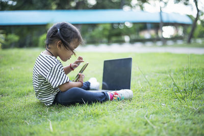 Side view of boy using digital tablet while sitting on field