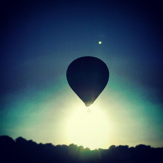 low angle view, sun, mid-air, flying, sky, blue, scenics, silhouette, hot air balloon, tranquility, clear sky, tranquil scene, lens flare, beauty in nature, copy space, nature, sunlight, sunbeam, outdoors, tree