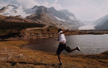 Full length of man throwing stone in lake by mountains 