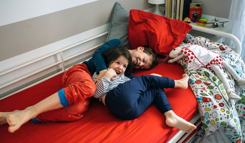 High angle view of siblings playing on bed at home