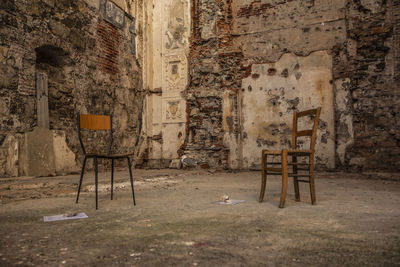 Empty chairs and table against wall in old building