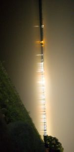 Illuminated street by road against sky at night