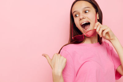 Portrait of young woman holding lollipop against pink background