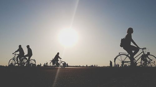 Silhouette people riding bicycle against sky