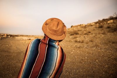 Rear view of person wearing hat while being wrapped in scarf on field against sky