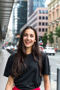 Portrait of smiling young woman standing against buildings in city