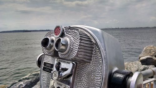 Close-up of coin-operated binoculars by sea against sky