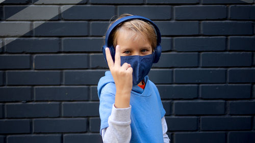 Portrait of boy wearing mask gesturing while standing against wall outdoors