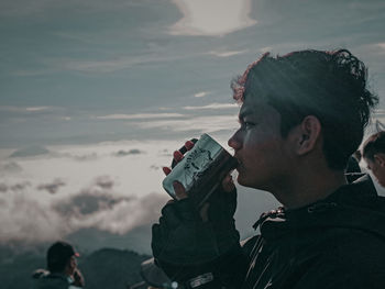 Portrait of young man drinking against sky