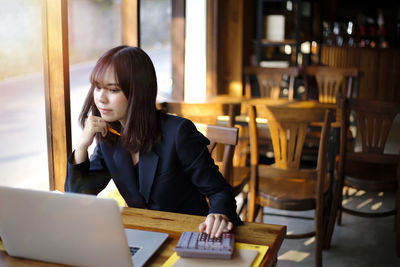 Businesswoman using calculator by laptop while sitting at table