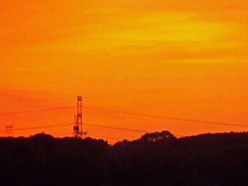 Silhouette electricity pylon against orange sky