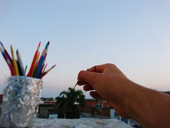 Cropped hand holding toothpick against sky