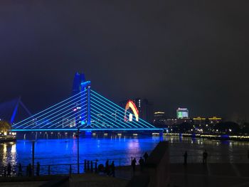 Illuminated bridge over river in city against sky at night