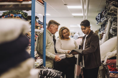 Multiracial fashion designers discussing while holding fabric at workshop