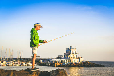 Boy fishing while standing by sea against sky