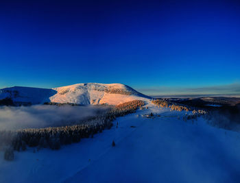 Aerial view of snowcapped mountain against blue sky