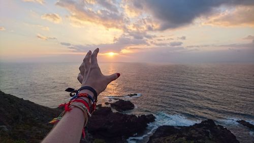 Cropped hand gesturing against sea during sunset