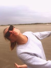 Portrait of woman wearing sunglasses on beach against sky