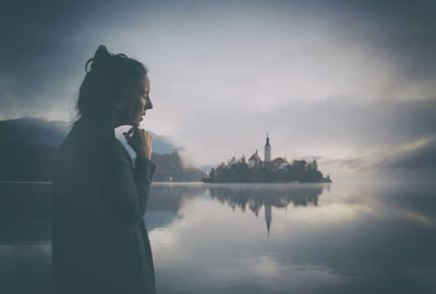 Woman in gray coat watching a sunrise among the fog on the shores of lake bled, slovenia