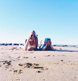 Mother and son lying on sand against clear sky at beach