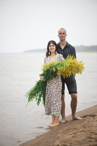 Young romantic couple with big bouquets of wild flowers posing on the beach