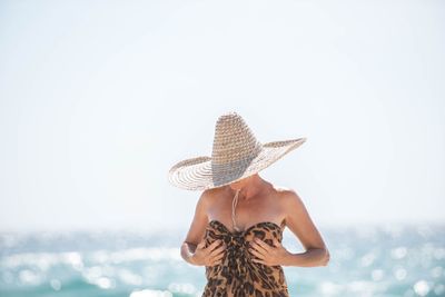 Woman wearing hat at beach against sky