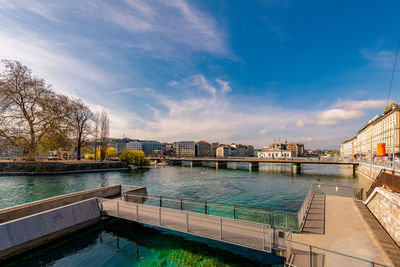 Bridge over river by buildings in city against sky