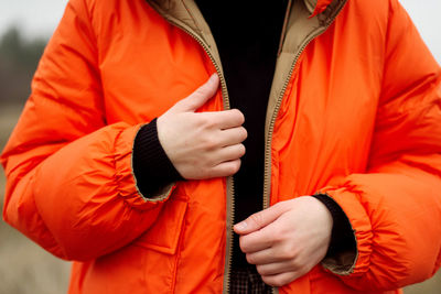 Unrecognizable female hands in bright orange jacket in winter