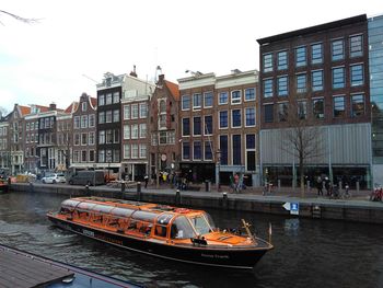 Boats moored on canal by buildings in city against sky