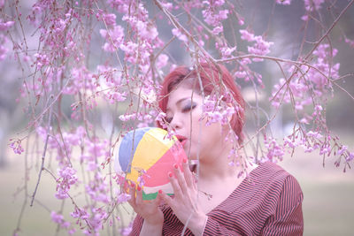 Young woman kissing colorful ball by flowering tree at park