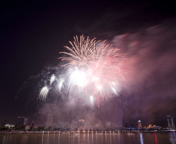 Low angle view of firework display over river against sky