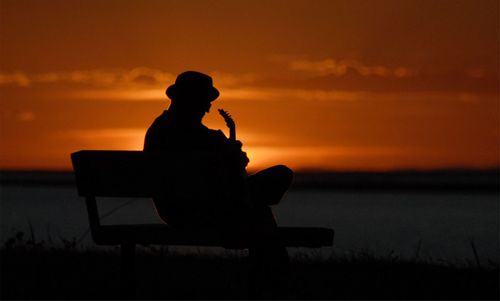 Silhouette man sitting by sea against sky during sunset