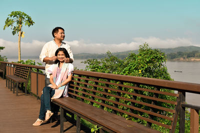 Front view of father and daughter at railing by sea against sky