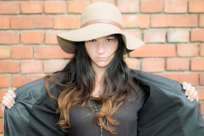 Portrait of beautiful young woman standing against brick wall