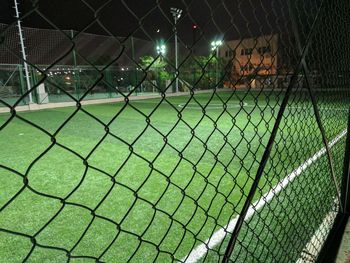 Close-up of green lights on field seen through chainlink fence