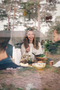 Happy young woman having lunch with friends seen through glass