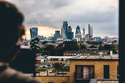 Rear view of man looking at cityscape against cloudy sky