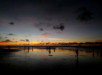 Silhouette people at beach against sky during sunset