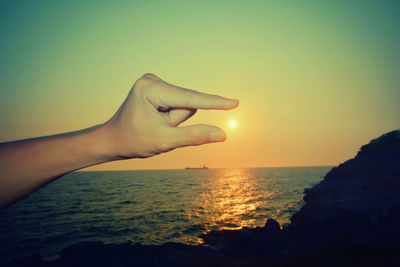Close-up of hand against sea during sunset