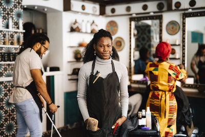 Portrait of confident young female hairdresser with hands in pockets at barber shop